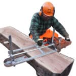 A man is working on a lumber using an Alaskan Mill.